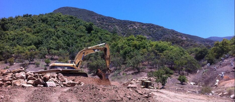 Excavator digging on gentle slope, with a hill in the background.